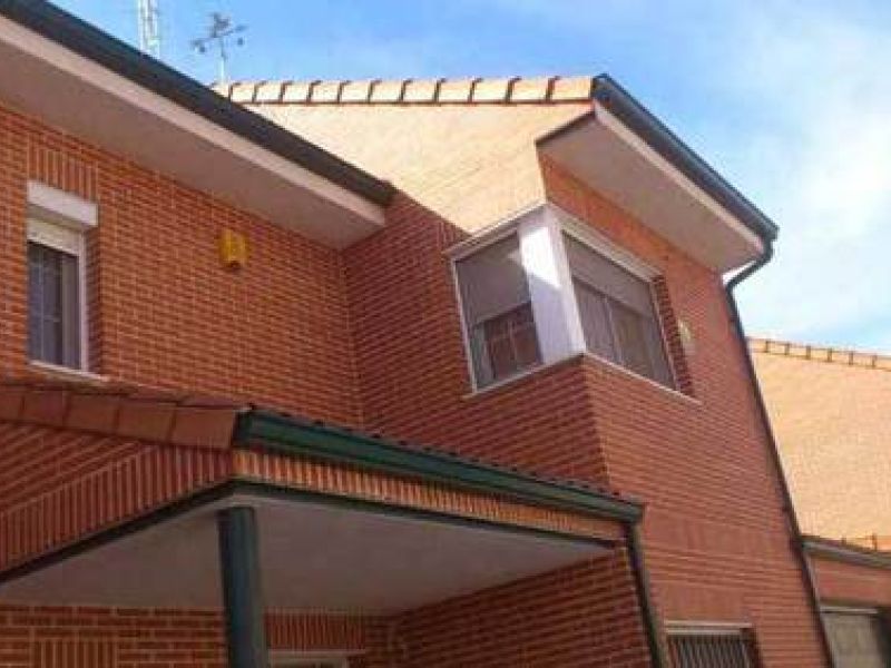 Canalón de chapa en tono verde descendiendo sobre fachada de chalet