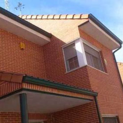 Canalón de chapa en tono verde descendiendo sobre fachada de chalet